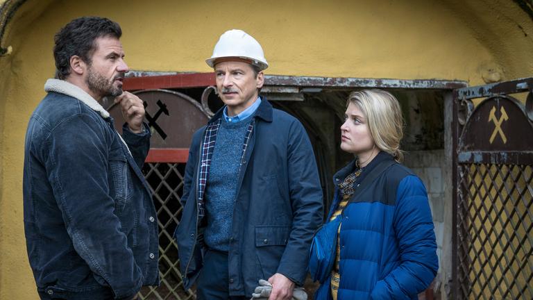 "Erzgebirgskrimi – Der Tote im Stollen": Adam (Stephan Luca) und Karina (Lara Mandoki) stehen zusammen mit Knut Erichsen (David Bunners) vor dem Eingang zu eines Stollens. Erichsen und Karina schauen zu Adam, der nachdenklich in die Ferne blickt.