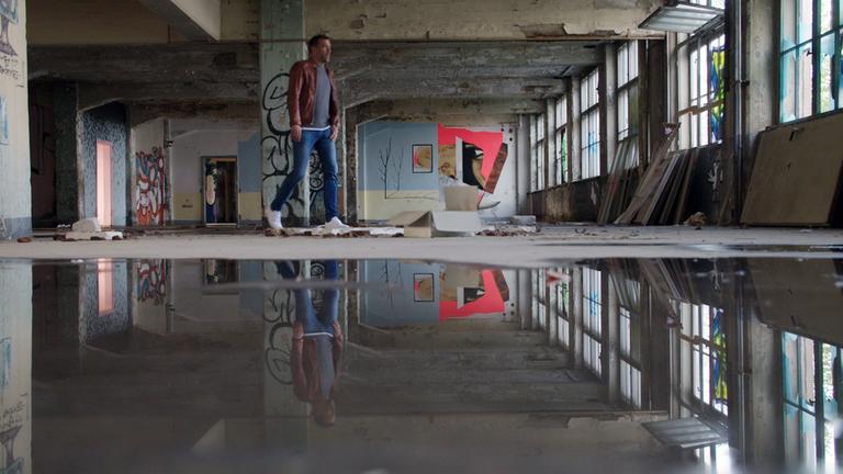 "WISO - Was sich im Osten verändert hat": Marcus Niehaves läuft durch eine leer stehende Lagerhalle. Teilweise sind die Fenster zerbrochen, Wasser steht auf dem Boden.