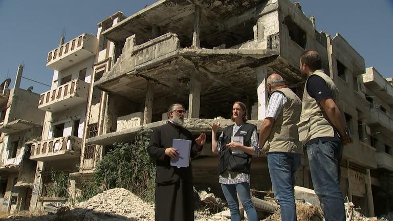 "ZDF.reportage Helfer in der Not - Katastrophenhilfe weltweit": Der Geistliche Dr. Alexi Chehadeh und Vera-Magdalena Voss von der Diakonie stehen in einem völlig zerstörten Stadtteil in Homs, Syrien.