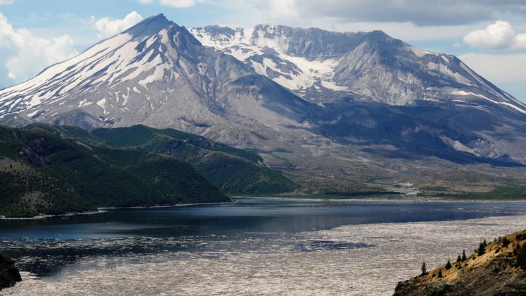 "Terra X: Feuer und Eis": Großer Berg mit stadionförmigem Krater, teils schneebedeckt. Im Vordergrund liegt ein See, in dem Baumstämme schwimmen.