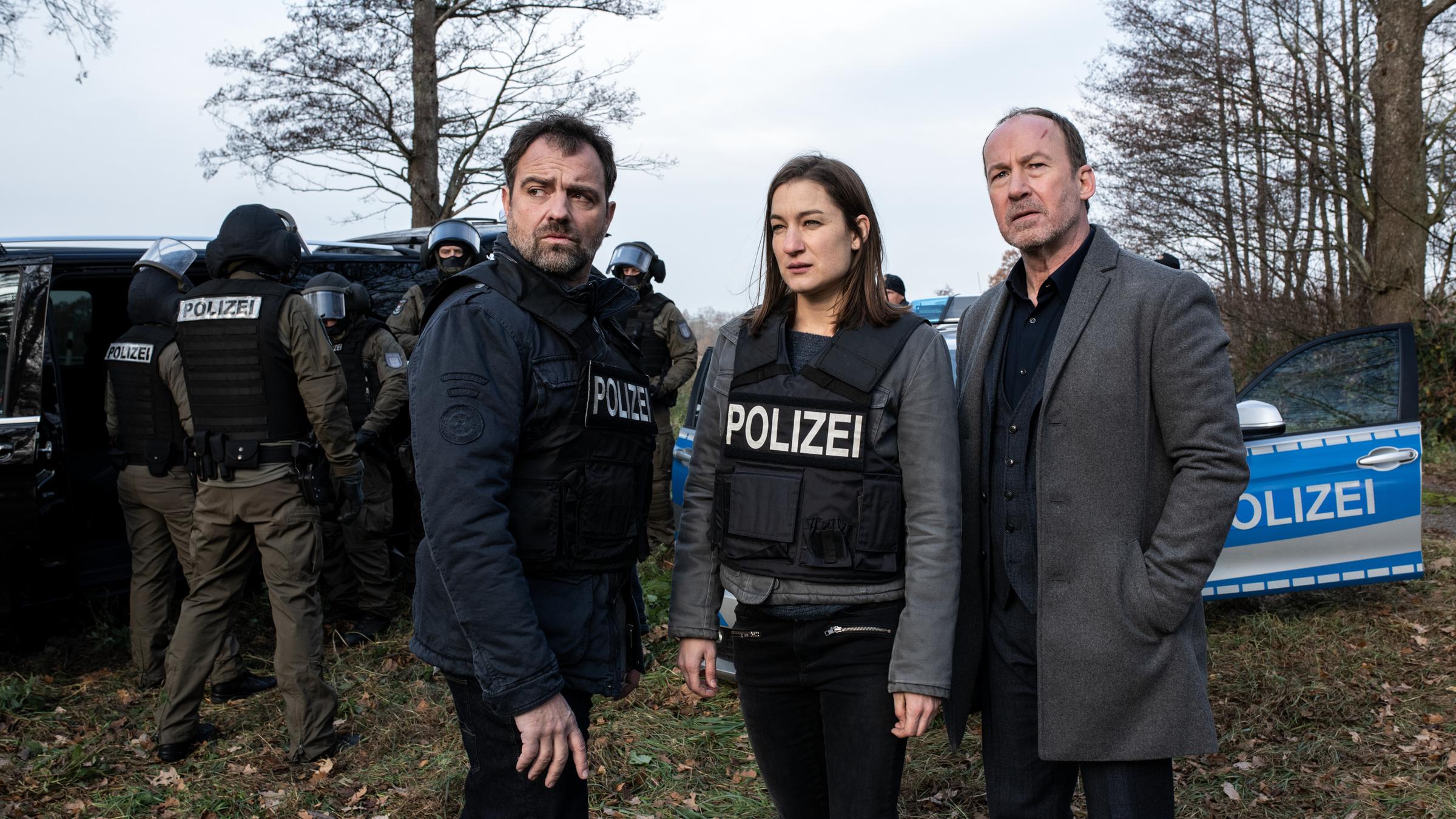 "Neben der Spur - Erlöse mich": Ruiz (Jürgen Maurer), Anna (Marie Leuenberger), Joe (Uli Noethen) stehen vor einem Polizeiwagen auf einer herbstgrauen Lichtung.