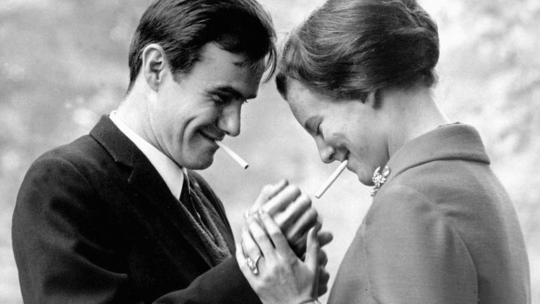 "ZDFzeit: Ein Leben für die Krone - Margrethe II. von Dänemark": Schwarz-weiß Aufnahme: Prinzgemahl Henrik zündet seiner jungen Frau, Königin Margrethe, eine Zigarette an. Beide lächeln und stehen sich vertraut gegenüber.