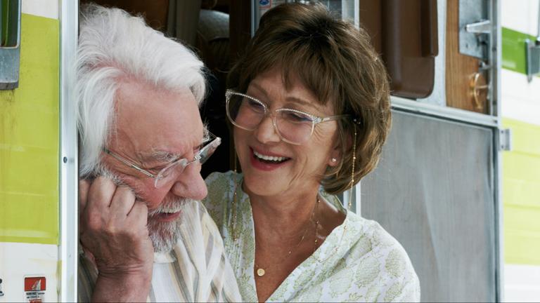 "Das Leuchten der Erinnerung": Ella (Helen Mirren) und John Spencer (Donald Sutherland) sitzen lachend, bei geöffneter Tür, auf den Eingangsstufen ihres Wohnmobils.