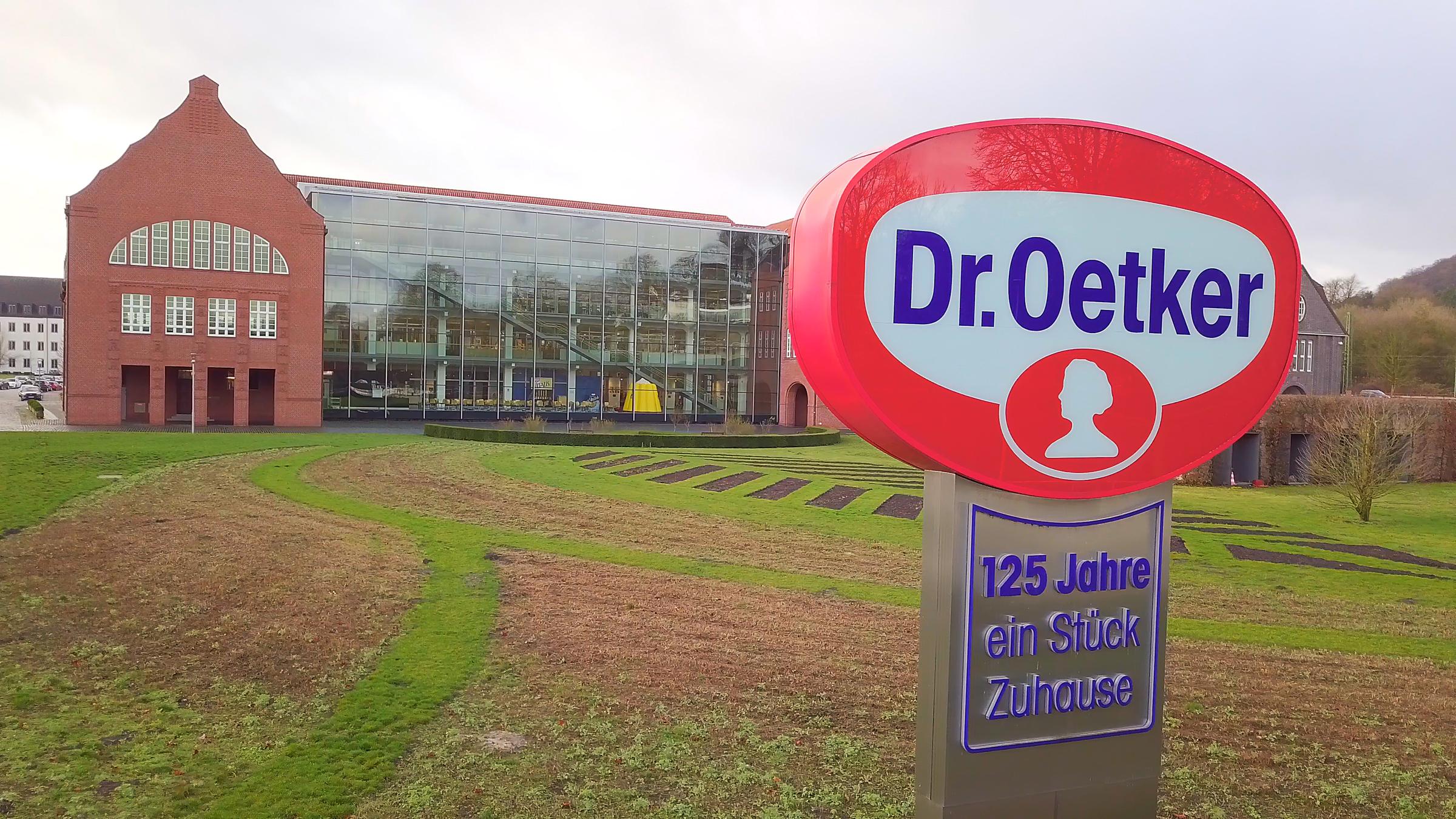 "ZDFzeit: Der große Dr. Oetker-Report - Wie gut sind Pudding, Pizza & Co.?": Konzernzentrale in Bielefeld mit Logo-Schild im Vordergrund.
