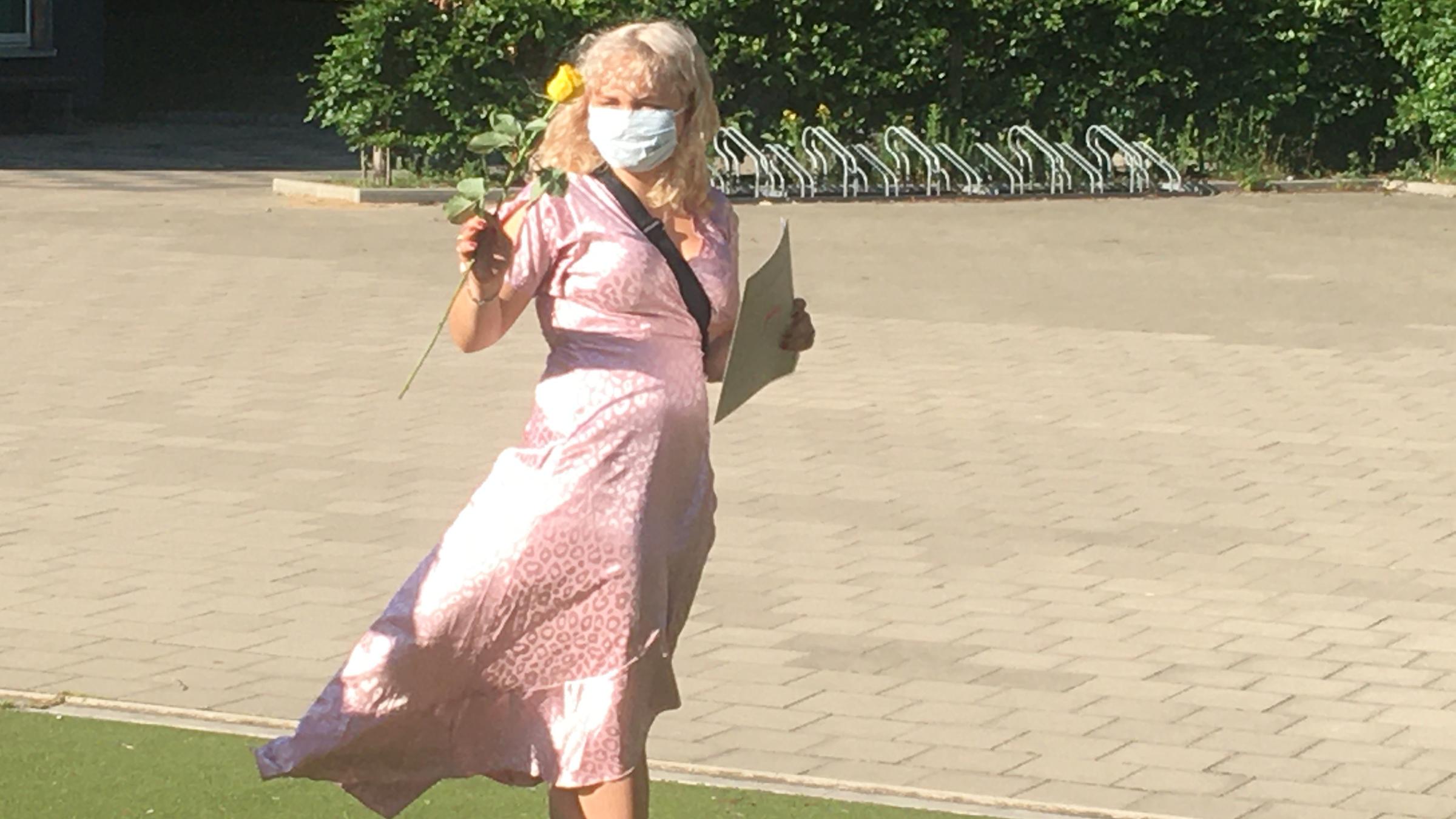 "37° Die Reifeprüfung - Erwachsen werden in schwierigen Zeiten": Zoe steht mit ihrem Zeugnis und einer Rose in der Hand im rosa Kleid vor ihrer Schule.