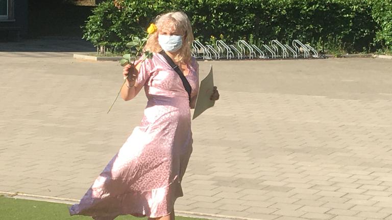 "37° Die Reifeprüfung - Erwachsen werden in schwierigen Zeiten": Zoe steht mit ihrem Zeugnis und einer Rose in der Hand im rosa Kleid vor ihrer Schule.