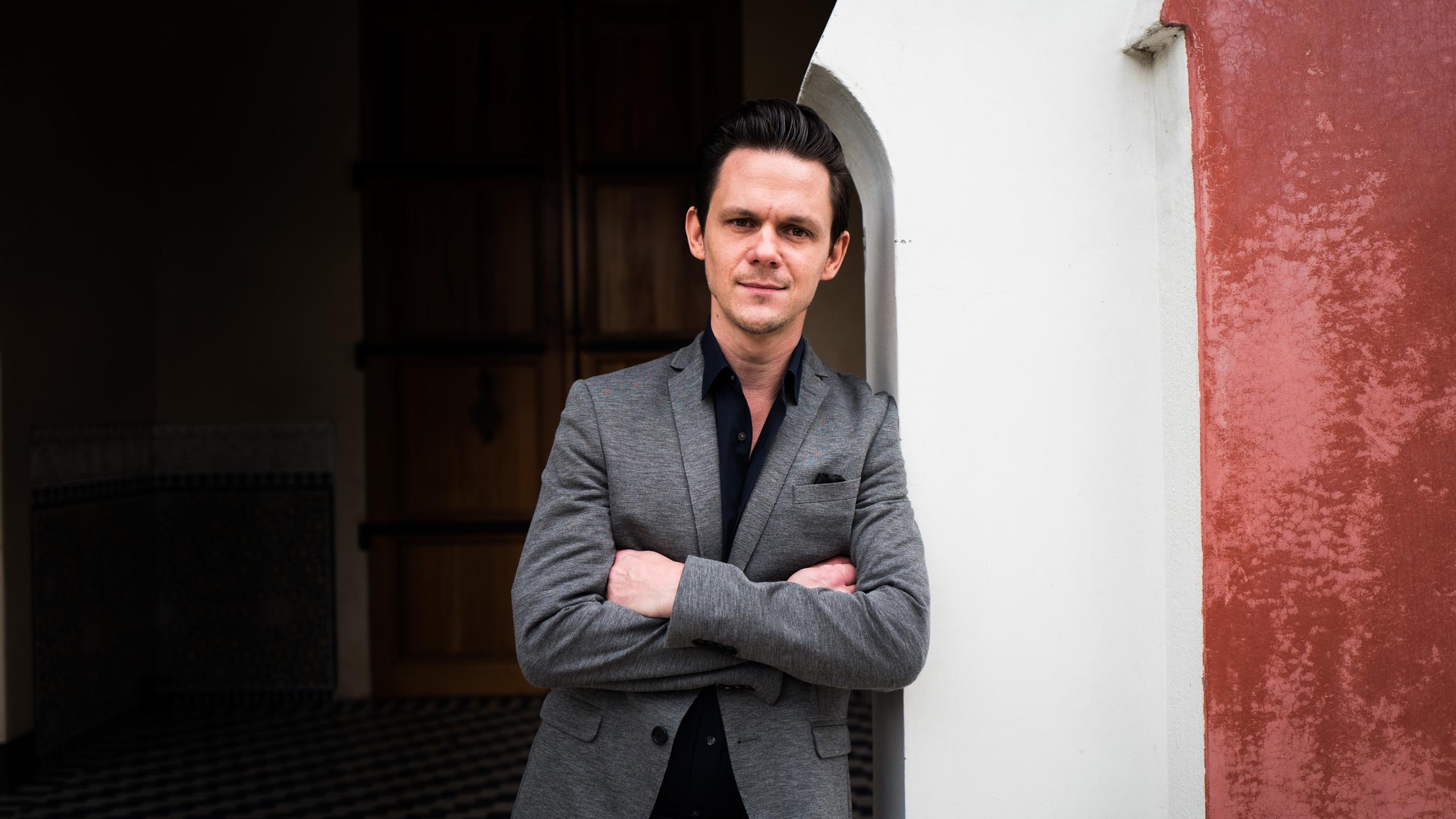 "Grimme-Preis 2020 - Die Reportage": Jo Schück lehnt mit verschränkten Armen an einer weißen Mauer.