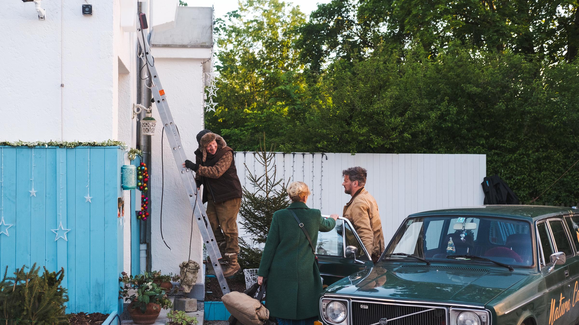 "Alle Nadeln an der Tanne": Kurt (Simon Schwarz) steigt von einer Leiter, die an der Hauswand lehnt. Er blickt zu seiner Frau Maria (Anna Loos) und ihrem Bruder Moritz (Marcus Mittermeier), die an der geöffneten Autotür stehen.