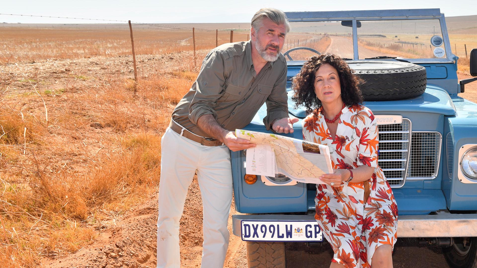 "Das Traumschiff Spezial": Daniel Morgenroth und Barbara Wussow im geblümten Kleid, dahinter blauer Landrover LR 88 in der Wüste.