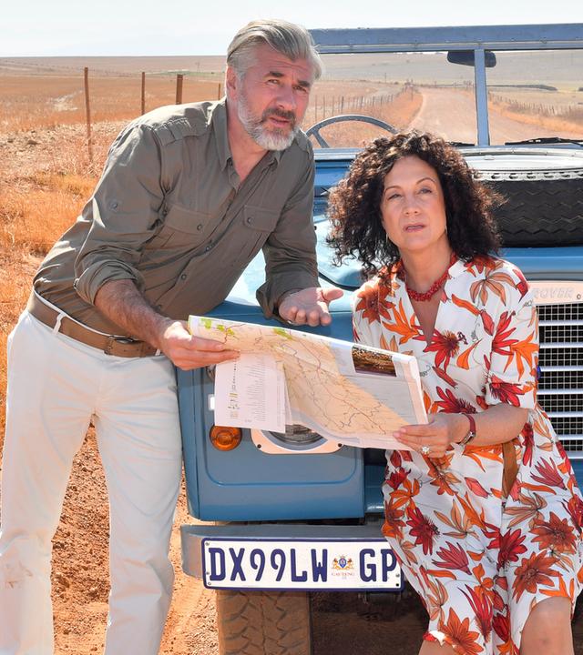 "Das Traumschiff Spezial": Daniel Morgenroth und Barbara Wussow im geblümten Kleid, dahinter blauer Landrover LR 88 in der Wüste.