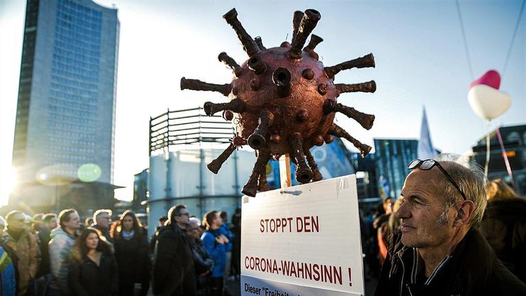 "ZDFzoom: Am Puls Deutschlands - Der Querdenker-Effekt – Kann uns Corona spalten?": Auf einer Demo in Leipzig steht ein Demonstrant mit einem Schild, das an einem Corona-Virus aus Plastik hängt. Auf dem Schild steht: "Stoppt den Corona-Wahnsinn!"