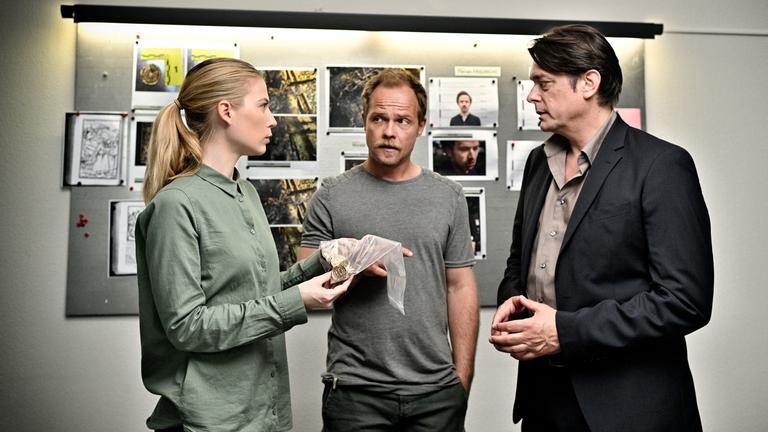 „Die Toten vom Bodensee - Fluch aus der Tiefe“: Hannah Zeiler (Nora Waldstätten), Michael Oberländer (Matthias Koeberlin) und Thomas Komlatschek (Hary Prinz) stehen im Büro beieinander und besprechen sich. Hannah hält einen Asservatenbeutel in ihren Händen.