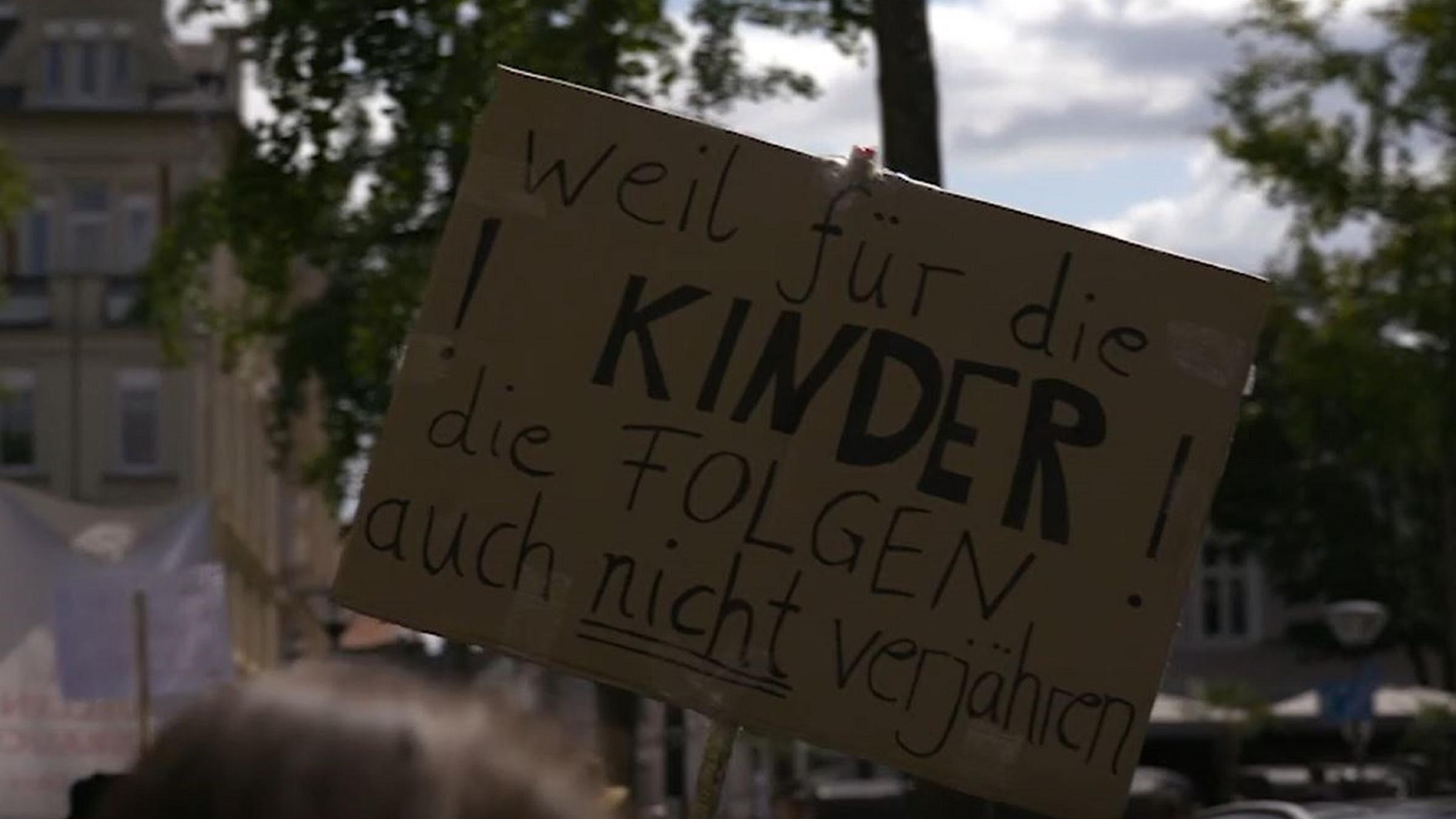  "Dunkelfeld - Kindesmissbrauch in Deutschland": Jemand hält ein Plakat aus Pappe hoch, auf dem steht: "weil für die Kinder die Folgen auch nicht verjähren".