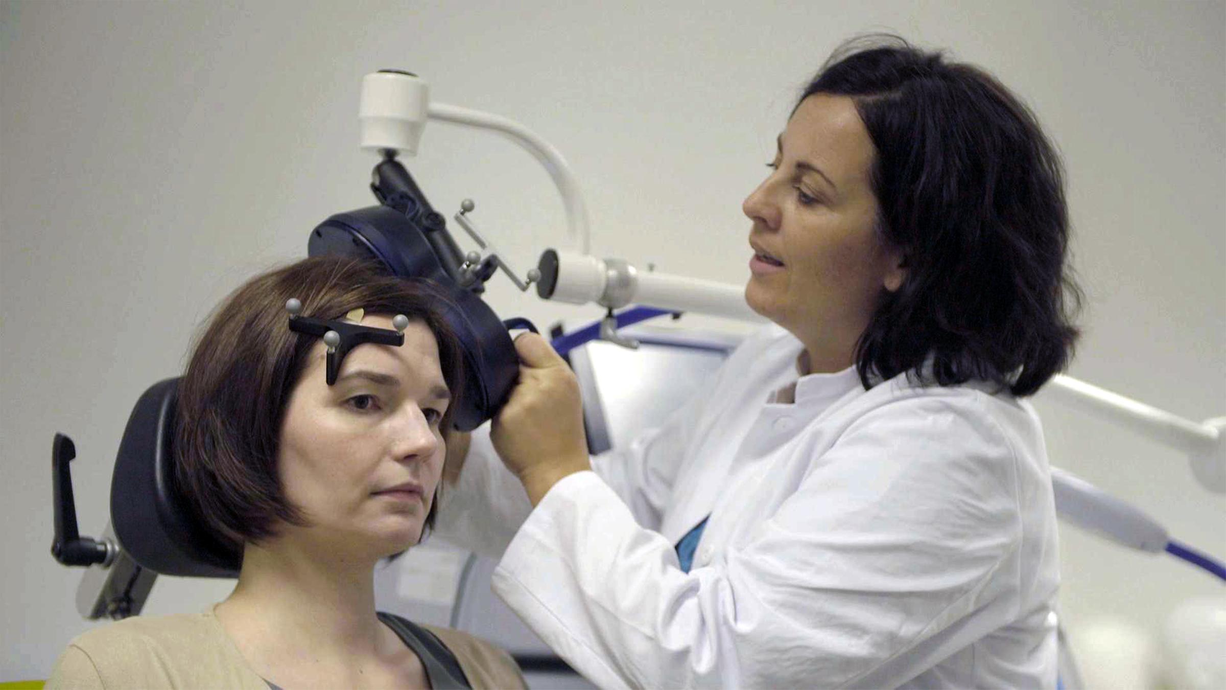 "Neustart für das Gehirn: Wege aus der Depression": Patientin und Ärztin im Behandlungsraum. Die Ärztin hält eine blaue Magnetspule an die linke Kopfseite der Patientin.