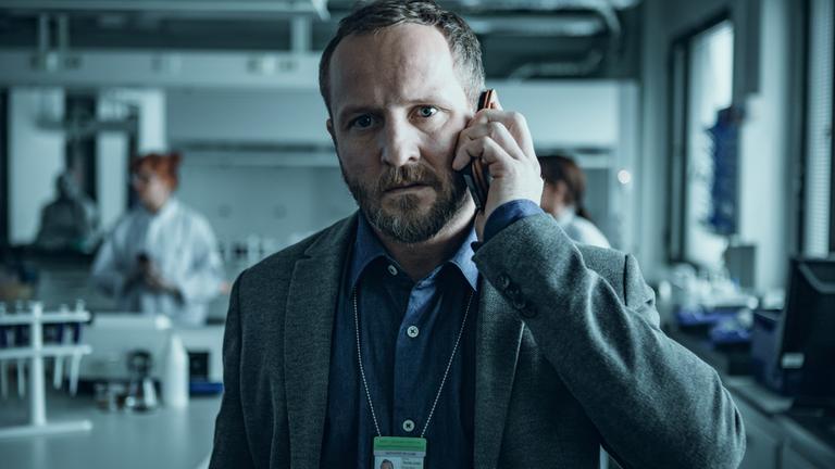 "Arctic Circle - Der unsichtbare Tod (1)": Dr. Thomas Lorenz (Maximilian Brückner) in Nahaufnahme. Er steht telefonierend in einem Labor.