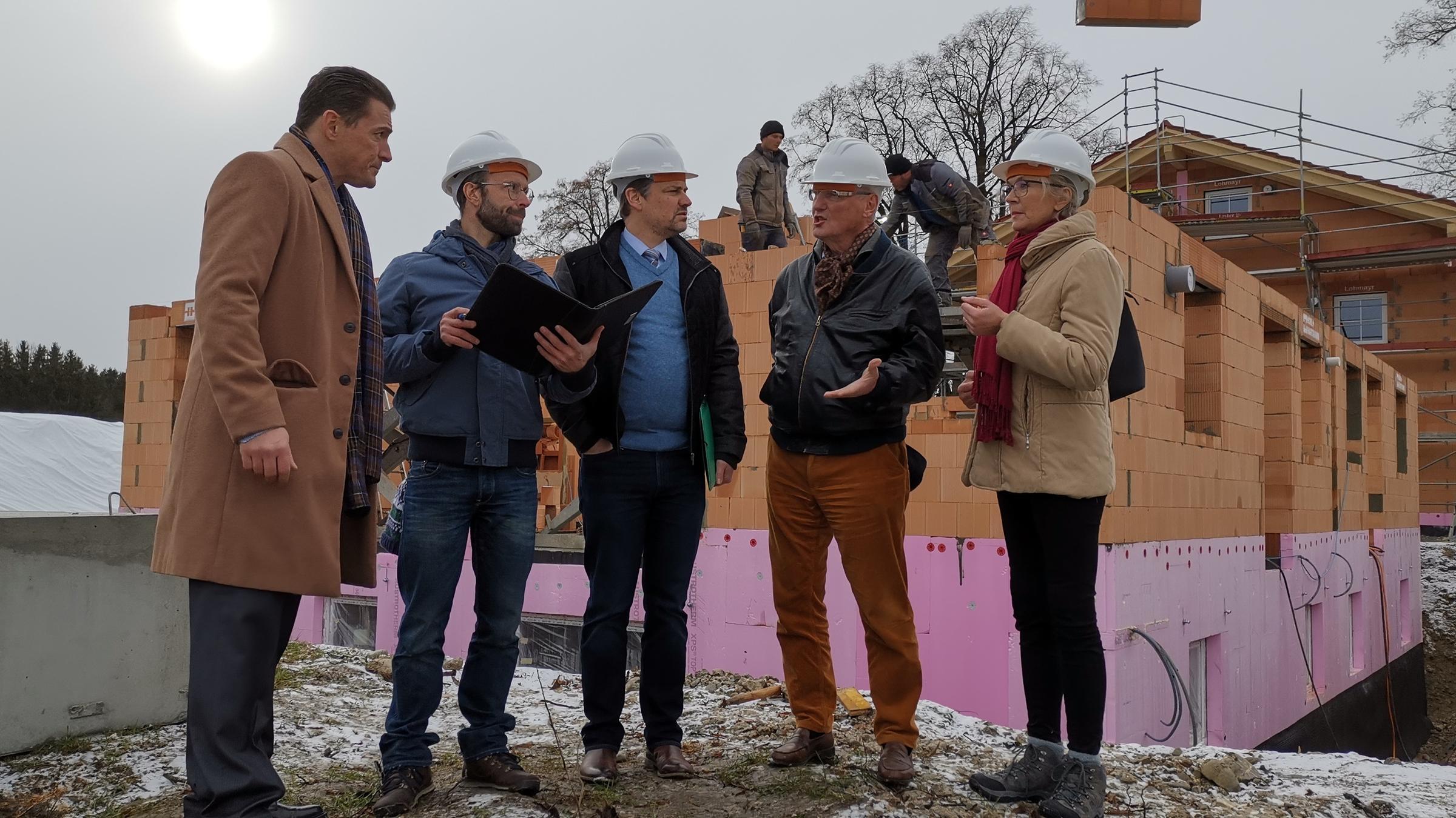 "Aktenzeichen XY-Spezial: Vorsicht, Betrug!": Auf einer Baustelle stehen vier Männer und eine Frau vor einem noch nicht fertig gestelltem Haus und diskutieren angeregt. Einer der Bauleute hält eine schwarze Mappe in den Händen.
