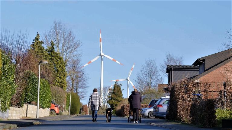 ZDFzoom: Das Ende der Energiewende? - Wie die Windkraft in Deutschland scheitert: Auf einer Straße gehen Frauen mit Hund und Rollator entlang. Im Hintergrund ragen Windräder auf.