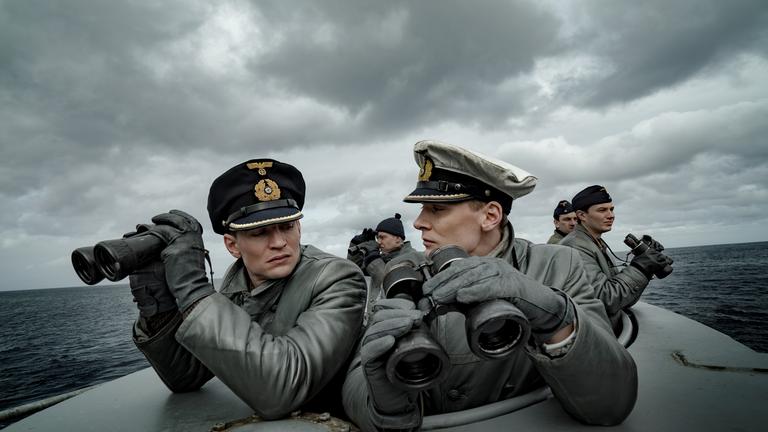 "Das Boot (1)":  Kapitänleutnant Klaus Hoffmann (Rick Okon) und sein 1. Wachoffizier Oberleutnant zur See Tennstedt (August Wittgenstein) haben Ferngläser in der Hand und sehen sich grimmig an. Sie befinden sich auf See und stehen in der Ausguck-Luke des U-Boots. Hinter ihnen stehen weitere Besatzungsmitglieder mit Ferngläsern.