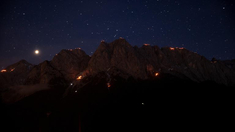  "Terra X: Deutschland bei Nacht - Land": Obere Bildhälfte Sternenhimmel über nächtlichen Berge. Oben auf den Bergen und mittig Feuer der Sonnwendfeiern.