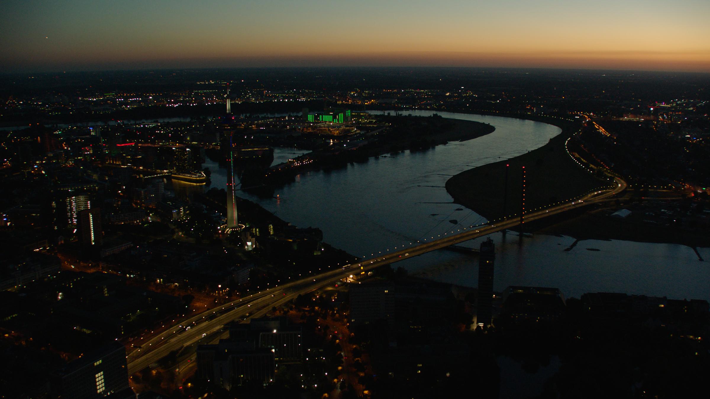 "Terra X: Deutschland bei Nacht - Stadt": Luftaufnahme von Düsseldorf. Deutlich erkennbar der Rhein. Und vorne im Bild eine beleuchtete Brücke über den Rhein.