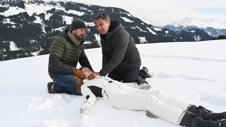 "Der Bergdoktor: Die dunkle Seite des Lichts": Natalie (Emilie Bernsdorf) liegt bewusstlos im Schnee. Ihr Vater Hannes (Simon Böer) und Dr. Martin Gruber (Hans Sigl) knien neben ihr und schauen besorgt.