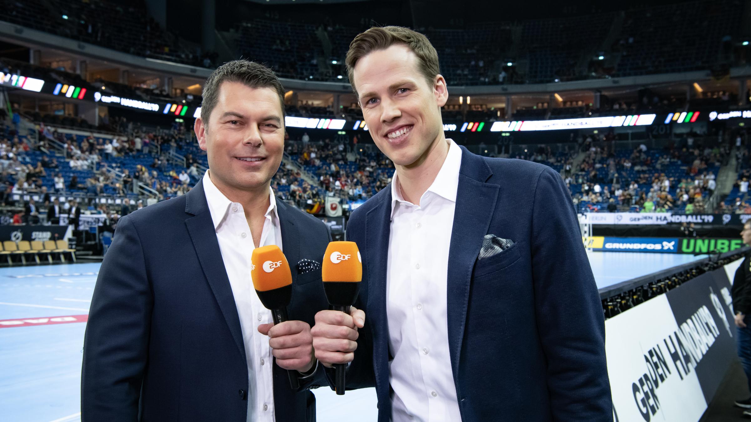 Yorck Polus und Sören Christophersen stehen mit Mikrofonen am Spielfeldrand in der Mecedes-Benz Arena in Berlin.