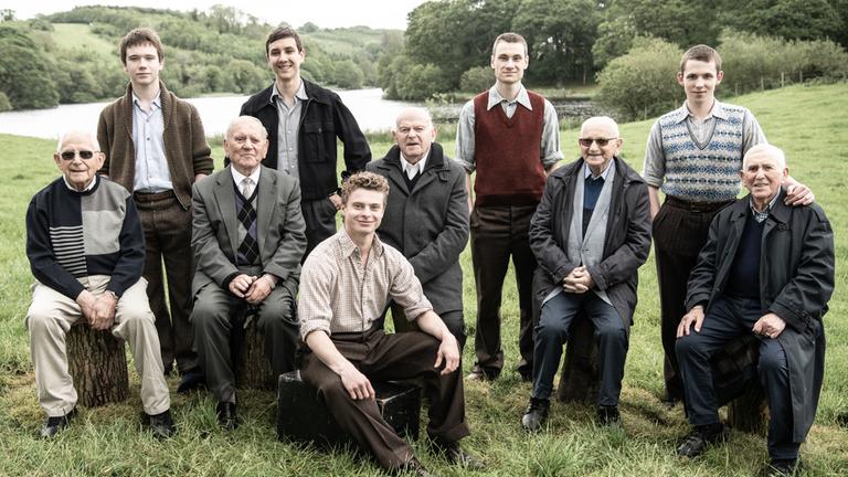"Die Kinder von Windermere": Chaim "Harry" Olmer, Kacper Swietek, Arek Hersh MBE, Tomasz Studzinski, Pascal Fischer, Sir Ben Helfgott, Schmuel "Sam Laskier", Marek Wroblewski, Icek "Ike" Alterman und Jakub Sprenger in einem Gruppenfoto. Sie sitzen und stehen auf einer Wiese und lächeln in die Kamera.