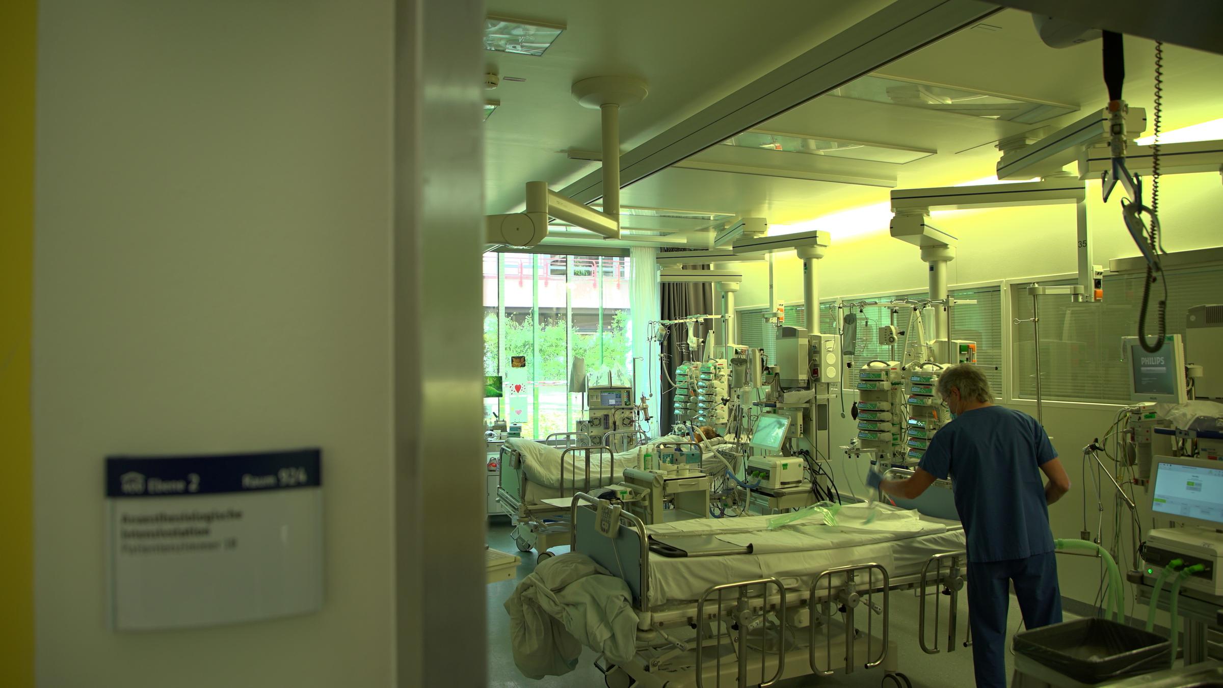 "ZDFzoom: Ärzte am Limit - Kostendruck statt Patientenwohl": Blick in ein Krankenzimmer mit zwei Krankenbetten. Am vorderen Bett steht ein Arzt in blauer Kleidung.