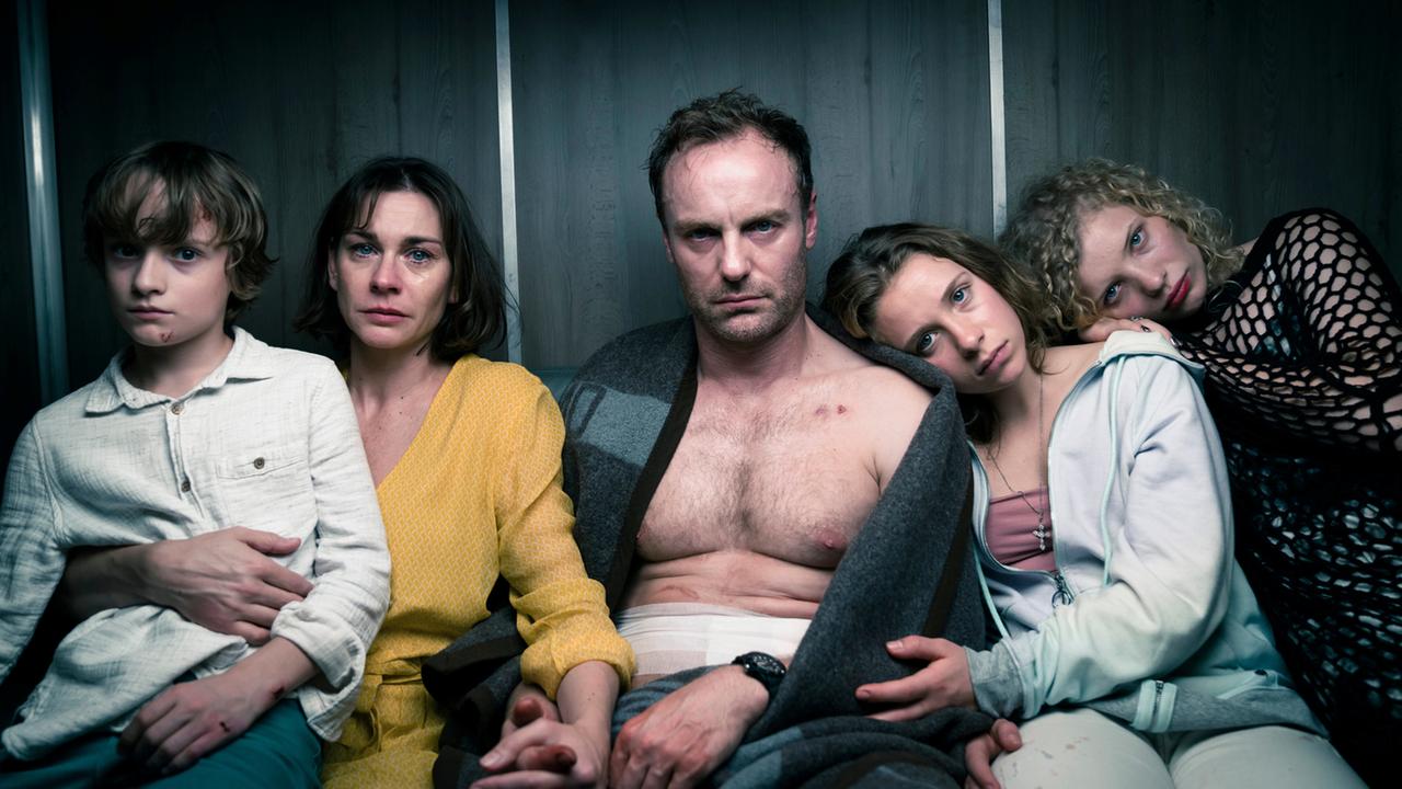 "8 Tage - Frieden": Familie Steiner: Jonas Steiner (Claude Heinrich), Susanne Steiner (Christiane Paul), Uli Steiner (Mark Waschke), Leonie Steiner (Lena Klenke) und Nora Frankenberg (Luisa-Céline Gaffron) sitzen mit traurigem Blick nebeneinander und halten sich im Arm oder an den Händen.