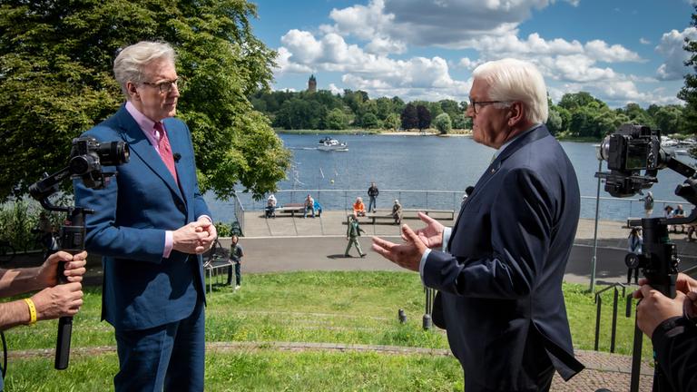 "Berlin direkt - Sommerintterview" 12. 7.2020: Theo Koll im Gespräch mit Frank-Walter Steinmeier. Sie stehen sich auf einer Wiese vor einem Seeufeer gegenüber.