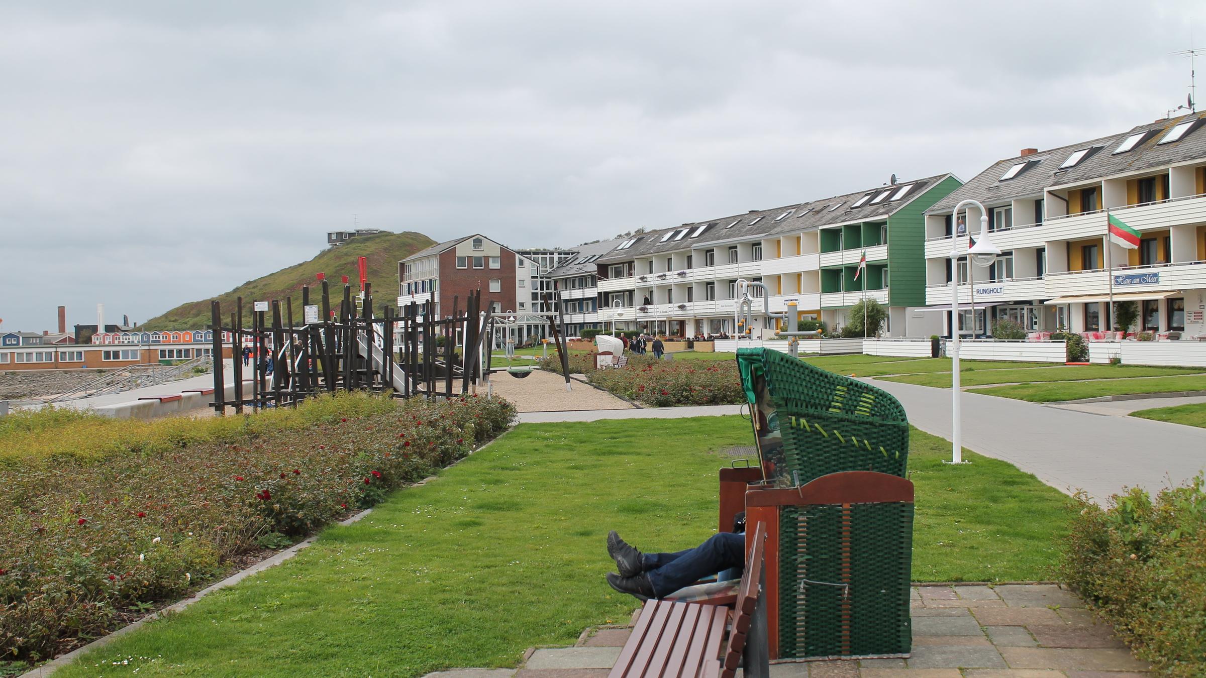 "ZDF.reportage: Robben, Schnaps und keine Gäste - Helgoland in der Krise": Aus einem Strandkorb an der Promenade schauen nur die Beine eines Urlaubers heraus. Im Hintergrund sind Strand, Spielplatz und Reihenhäuser zu sehen.