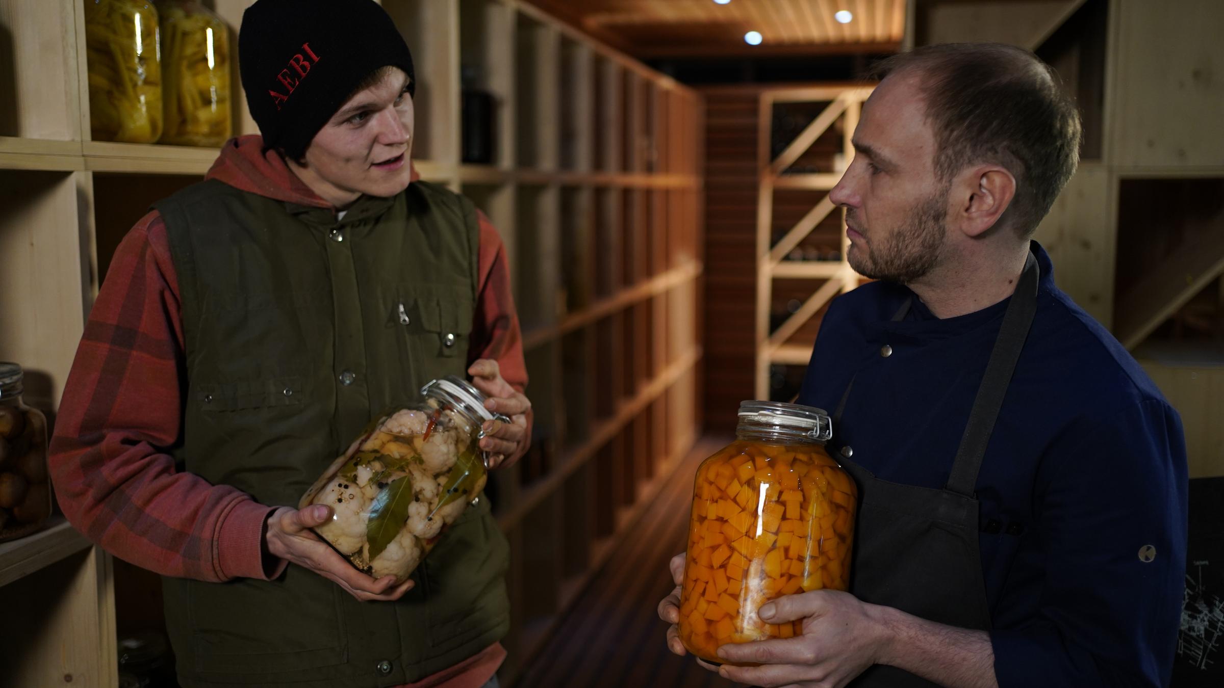 "plan b: Wirtschaft, die gut tut - Wie Unternehmen die Zukunft planen": Christoph Kaufmann und Nico Hirschfeld stehen mit Einmachgläsern in der Hand in einem Vorratskeller und unterhalten sich.