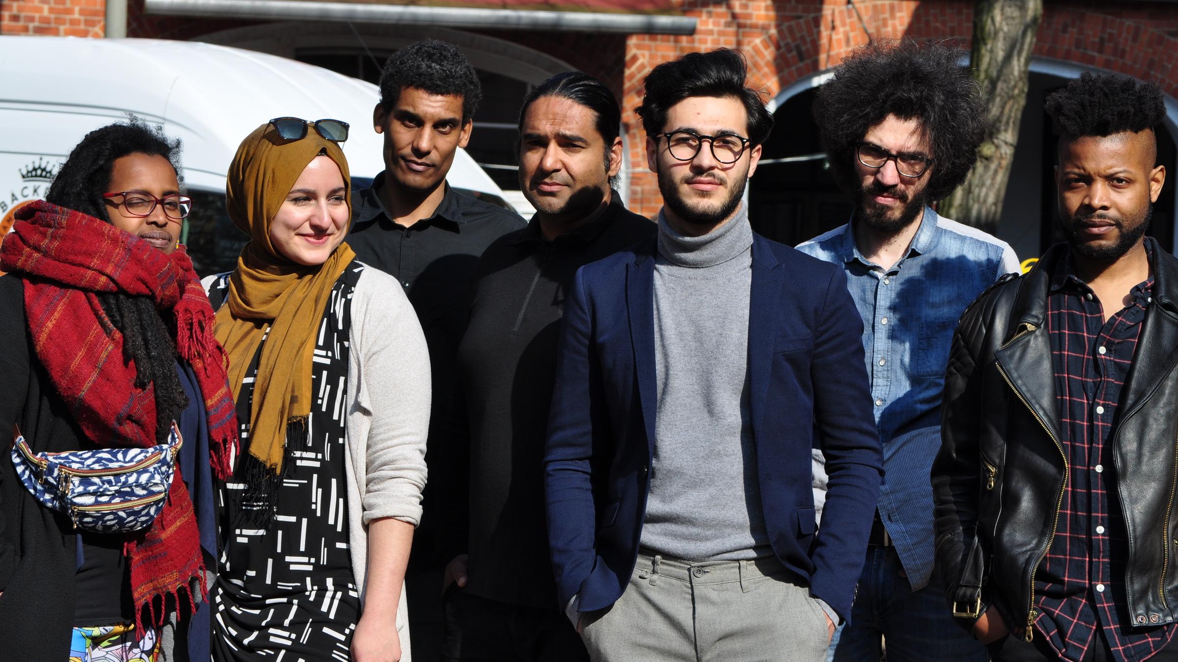 "ZDFzeit: Streitfall Rassismus - Wie gleich sind wir?": Eine Gruppe von sieben jungen Erwachsenen, 2 Frauen und 5 Männern, steht im Sonnenlicht vor einem roten Backsteingebäude.