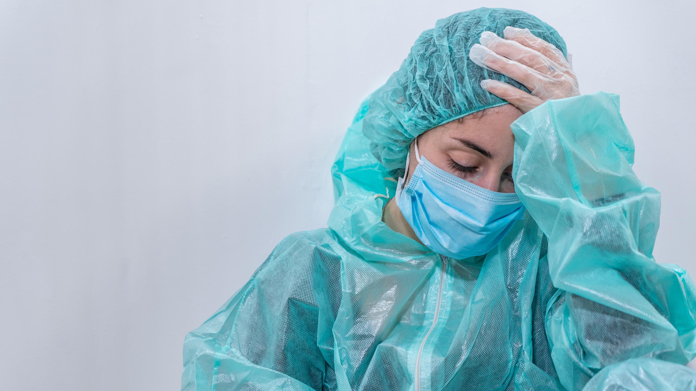 "Corona 2020 - Der Ausbruch - Schock und Versagen": Eine Frau in blauer Schutzkleidung sitzt erschöpft auf dem Boden.