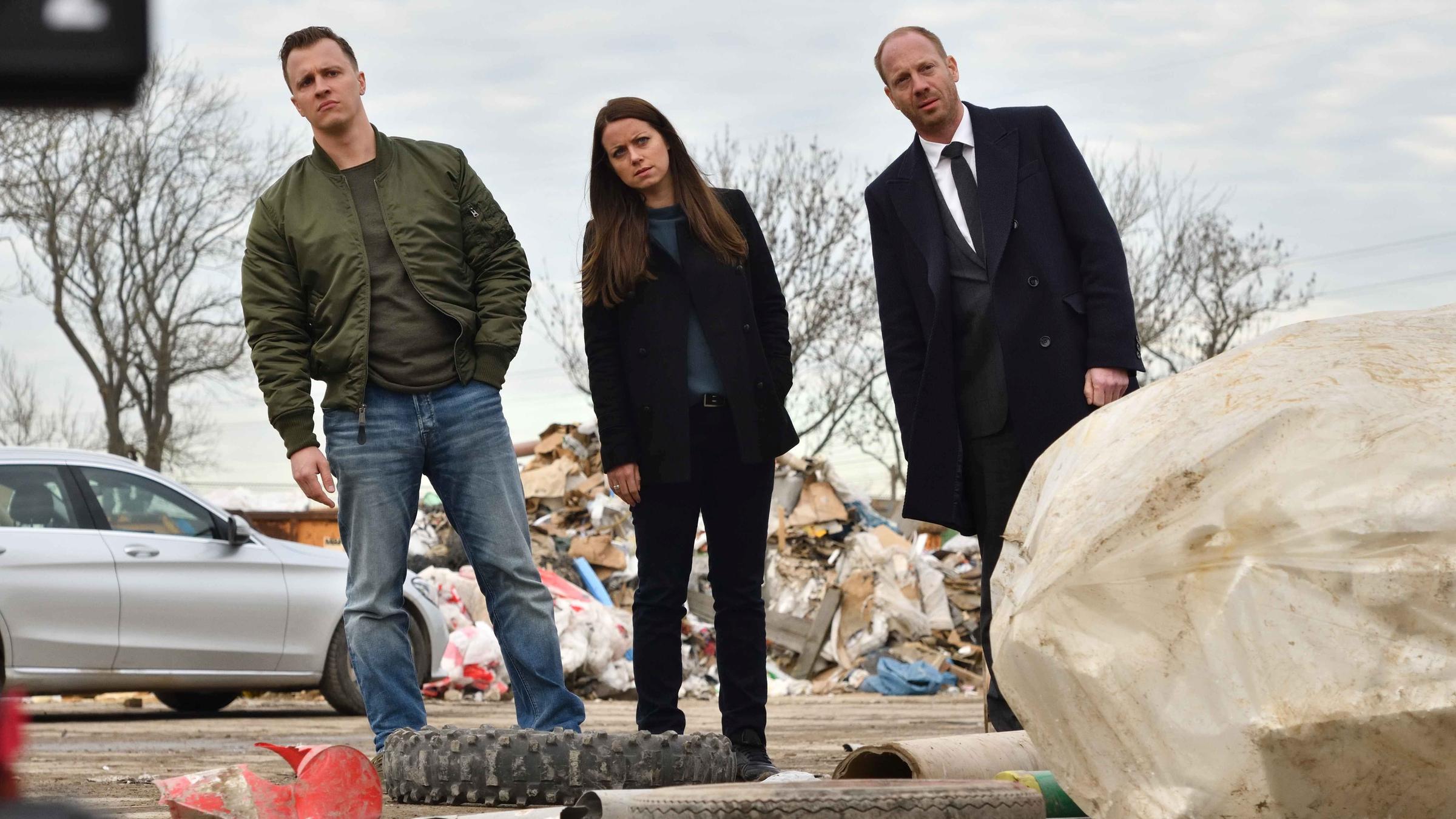 "Herr und Frau Bulle – Abfall": Yvonne (Alice Dwyer), Heiko (Johann von Bülow), und Kevin (Tim Kalkhof) stehen in einer Reihe auf einer Mülldeponie und neigen sich alle nach links.