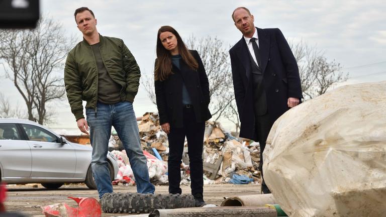"Herr und Frau Bulle – Abfall": Yvonne (Alice Dwyer), Heiko (Johann von Bülow), und Kevin (Tim Kalkhof) stehen in einer Reihe auf einer Mülldeponie und neigen sich alle nach links.