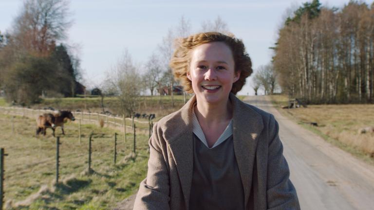 "Astrid": Die 16-jährige Astrid (Alba August) fährt mit dem Fahrrad durch eine ländliche Gegend, an Pferdekoppeln vorbei, und strahlt über das ganze Gesicht.