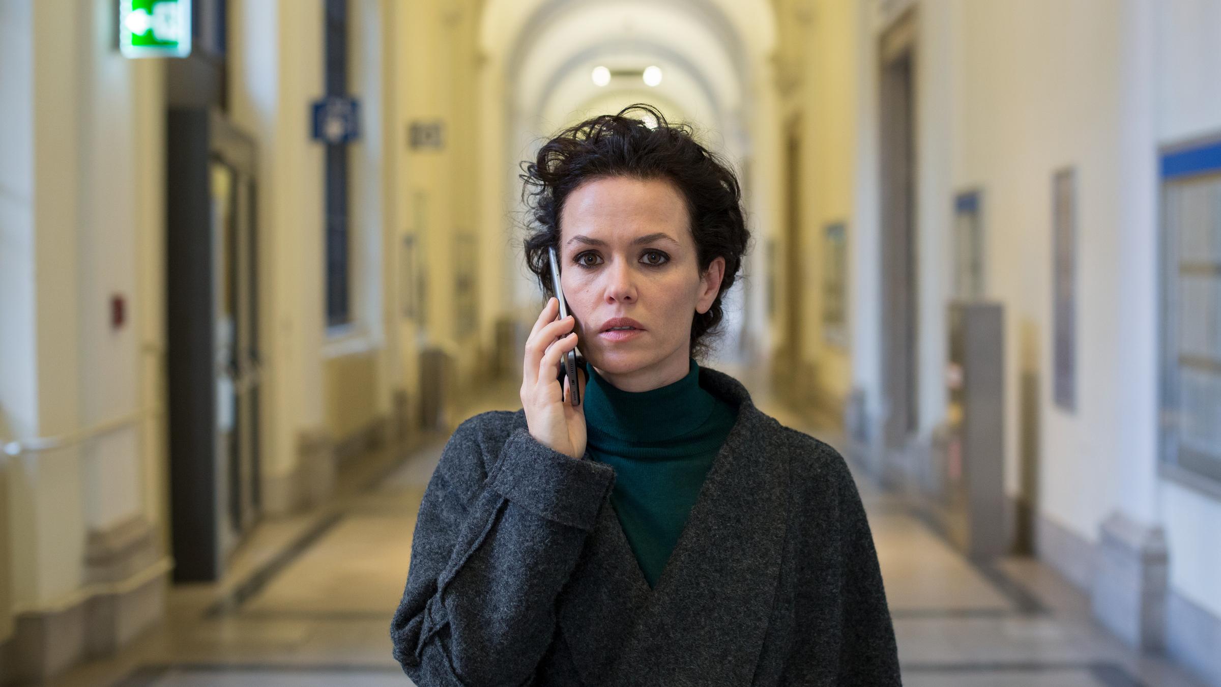 "Wiener Blut": Fida Emam (Melika Foroutan) steht in einem langen Flur mit einer hohen gewölbten Decke. Sie hält sich ihr Smartphone ans Ohr und blickt besorgt geradeaus.