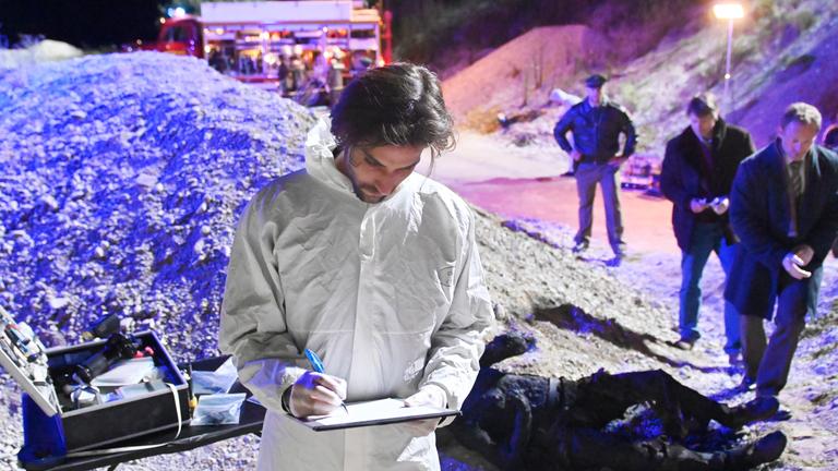 "Aktenzeichen XY-Spezial: Cold Case": Eine Leiche liegt auf einer Lavagrube. Ein Mann im weißen Schutzanzug notiert den Befund. Ein Polizist und zwei weitere Männer stehen seitlich zur Leiche.