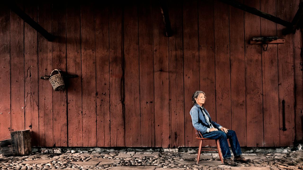 "Alters Land": Vera Eckhoff (Iris Berben) sitzt auf einem Stuhl vor einer hölzernen Scherunenwand und schaut in die Ferne.