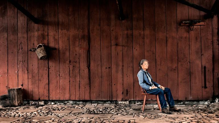 "Alters Land": Vera Eckhoff (Iris Berben) sitzt auf einem Stuhl vor einer hölzernen Scherunenwand und schaut in die Ferne.