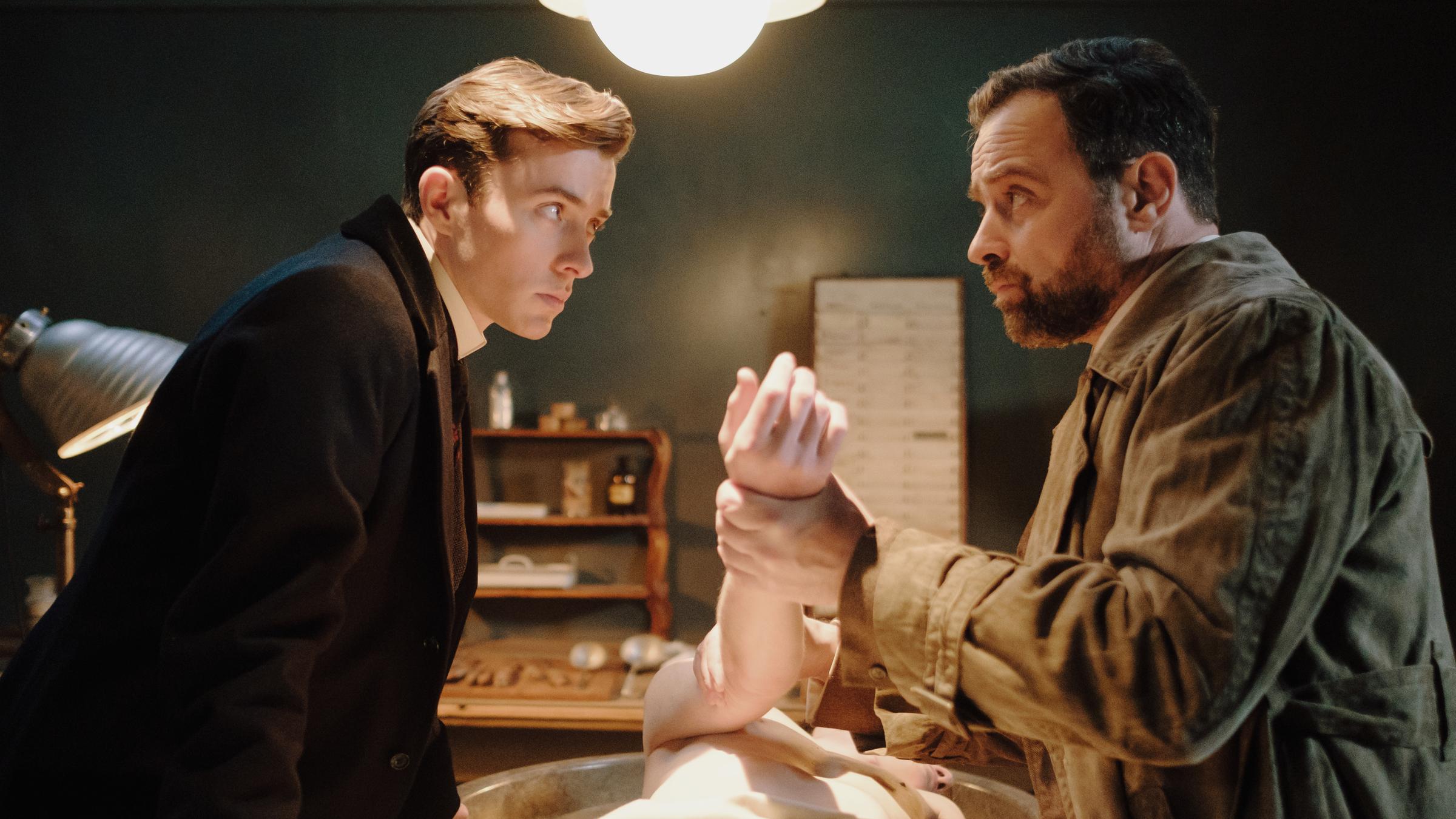 "Vienna Blood - Der verlorene Sohn": Max (Matthew Beard, l.) und Oskar (Juergen Maurer, r.) stehen vor einer Leiche, die mittig auf einem Tisch liegt.