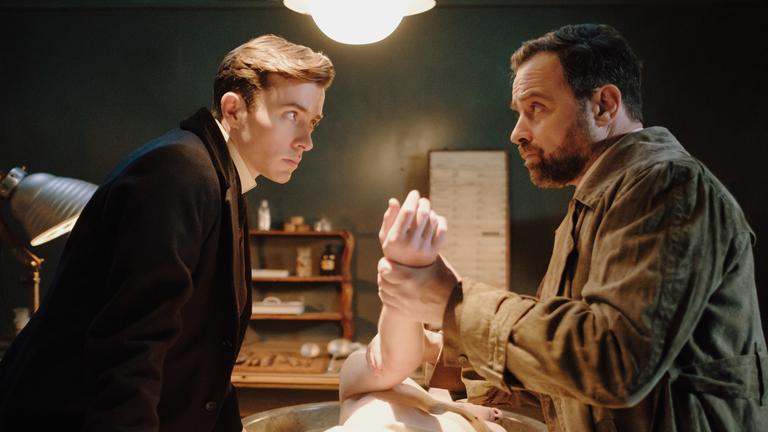"Vienna Blood - Der verlorene Sohn": Max (Matthew Beard, l.) und Oskar (Juergen Maurer, r.) stehen vor einer Leiche, die mittig auf einem Tisch liegt.