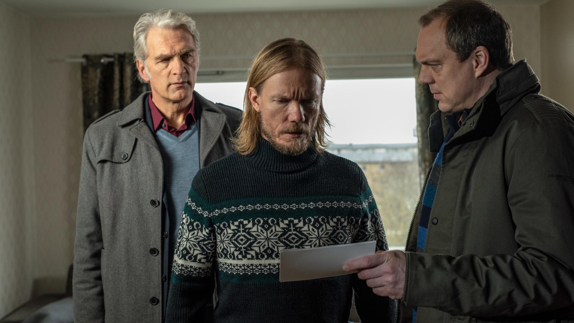 "Der Kommissar und das Meer - Aus glücklichen Tagen": Thomas (Andy Gätjen) hält Sigge (Matti Boustedt) ein Foto unter die Augen, während Robert (Walter Sittler) hinter Sigge steht und ihn argwöhnisch beobachtet.