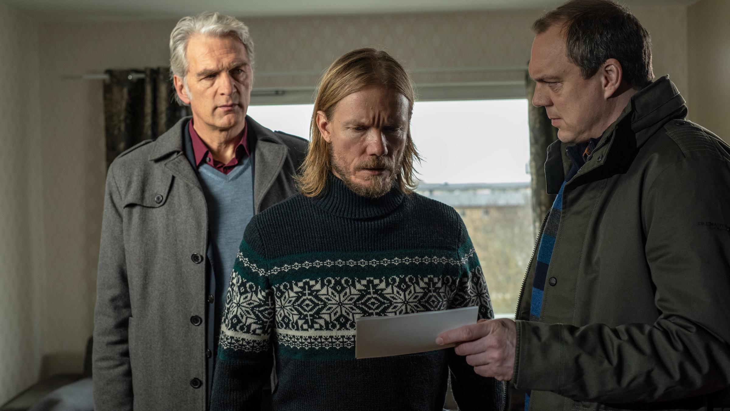 "Der Kommissar und das Meer - Aus glücklichen Tagen": Thomas (Andy Gätjen) hält Sigge (Matti Boustedt) ein Foto unter die Augen, während Robert (Walter Sittler) hinter Sigge steht und ihn argwöhnisch beobachtet.