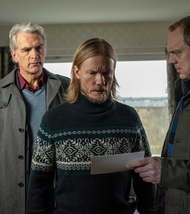 "Der Kommissar und das Meer - Aus glücklichen Tagen": Thomas (Andy Gätjen) hält Sigge (Matti Boustedt) ein Foto unter die Augen, während Robert (Walter Sittler) hinter Sigge steht und ihn argwöhnisch beobachtet.