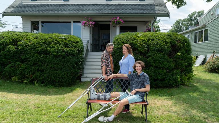 "Katie Fforde: Für immer Mama": Marc (Alexander Wipprecht) und Helen (Rebecca Immanuel) stehen zusammen vor ihrem Haus, Louis (Jascha Baum) sitzt mit Krücken auf der Bank vor ihnen.