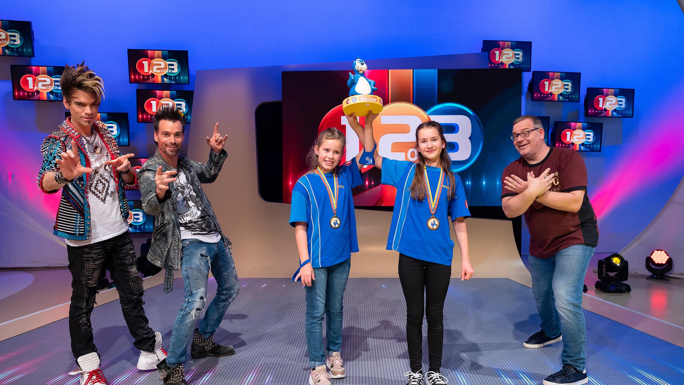 "1, 2 oder 3 - Elton & Friends": Die Kandidatinnen aus Bernau/Deutschland halten gemeinsam den Piet-Flosse-Pokal in die Höhe. Links von ihnen stehen die Ehrlich Brothers und rechts Moderator Elton.