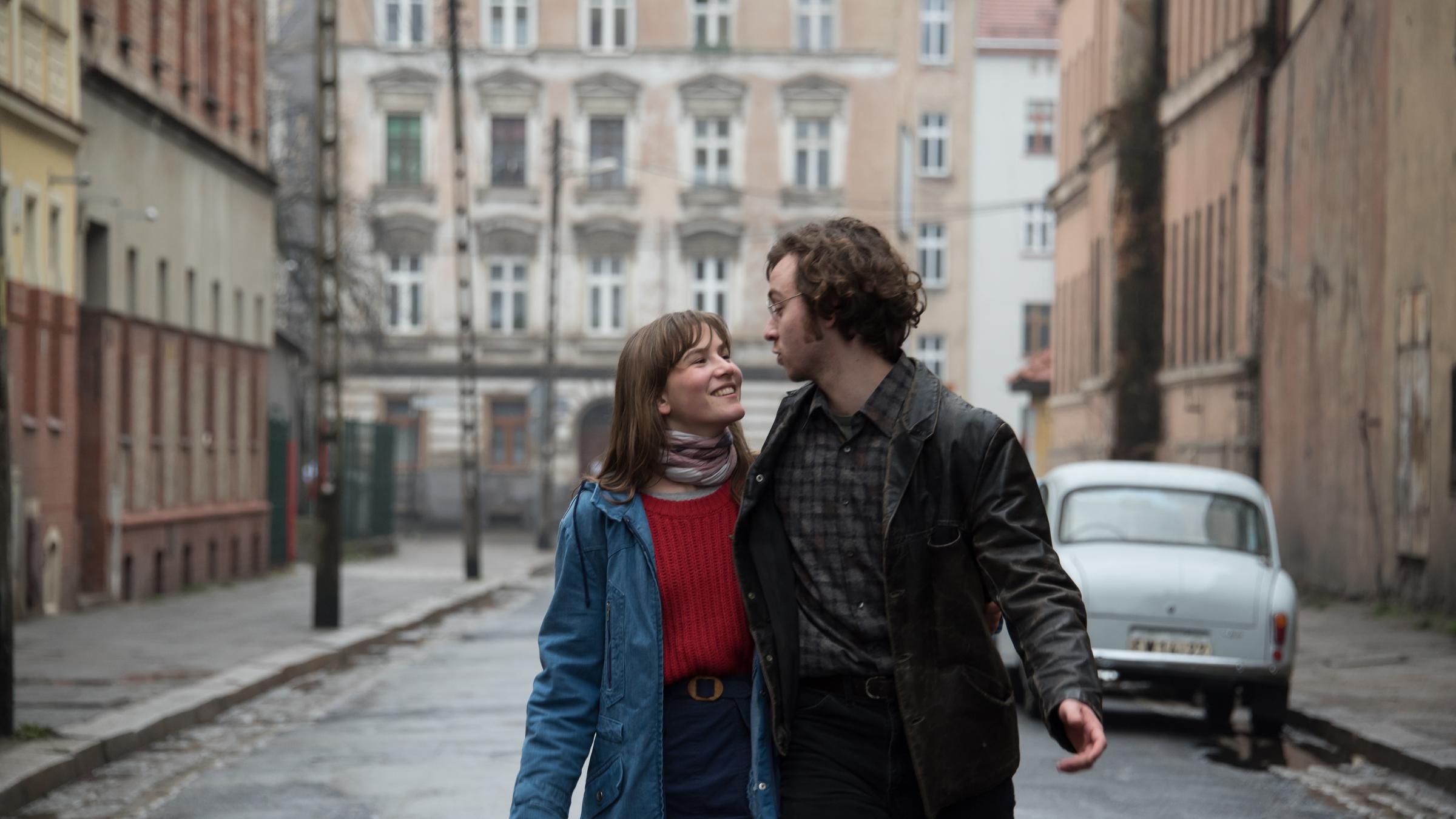  "Zwischen uns die Mauer": Anna (Lea Freund) und Philipp (Tim Bülow) laufen Arm in Arm durch eine Straße mit typischen Mietshäusern aus Ostberlin. Sie sehen sich verliebt in die Augen.