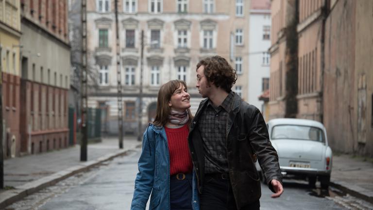  "Zwischen uns die Mauer": Anna (Lea Freund) und Philipp (Tim Bülow) laufen Arm in Arm durch eine Straße mit typischen Mietshäusern aus Ostberlin. Sie sehen sich verliebt in die Augen.